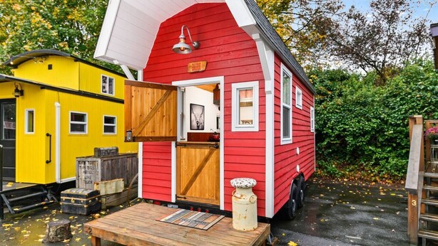 Una casa móvil roja con techo blanco, una puerta de madera y un pequeño porche.