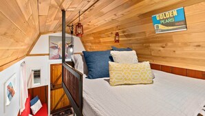 Una habitación acogedora con techo de madera, una cama con almohadones estampados, un cuadro en la pared y un cartel de Golden Pears.