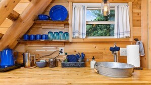 A wooden kitchen with blue and green glassware, a metal sink, and a 'SUPPLIES' container.