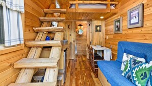 A log cabin interior with a wooden staircase, a dining area, and a blue sofa with patterned cushions.