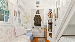 A cozy room with a floral-patterned sofa, a wooden floor, and a window with decorative plates. - The Cottage - Custom Tiny Home w/ Victorian Vibe (Portland)