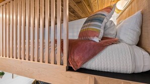 A wooden crib with a slatted design, a white quilted mattress, and a striped pillow. - The Finlandia - Custom Tiny Home w/ Finnish Vibe (Portland)
