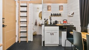 A compact kitchen with a built-in stove, a sink, and a small dining area with chairs. - The Finlandia - Custom Tiny Home w/ Finnish Vibe (Portland)