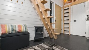 A modern interior with a black sofa, a colorful striped pillow, a black heater, a wooden ladder, and a white door with shelves. - The Finlandia - Custom Tiny Home w/ Finnish Vibe (Portland)