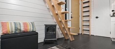 Ein modernes Interieur mit einem schwarzen Sofa, einem farbenfrohen gestreiften Kissen, einem schwarzen Heizkörper, einer Holzleiter und einer weißen Tür mit Regalen.