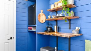 Cocina compacta con paredes azules, encimera de madera, hervidor y un taburete pequeño.