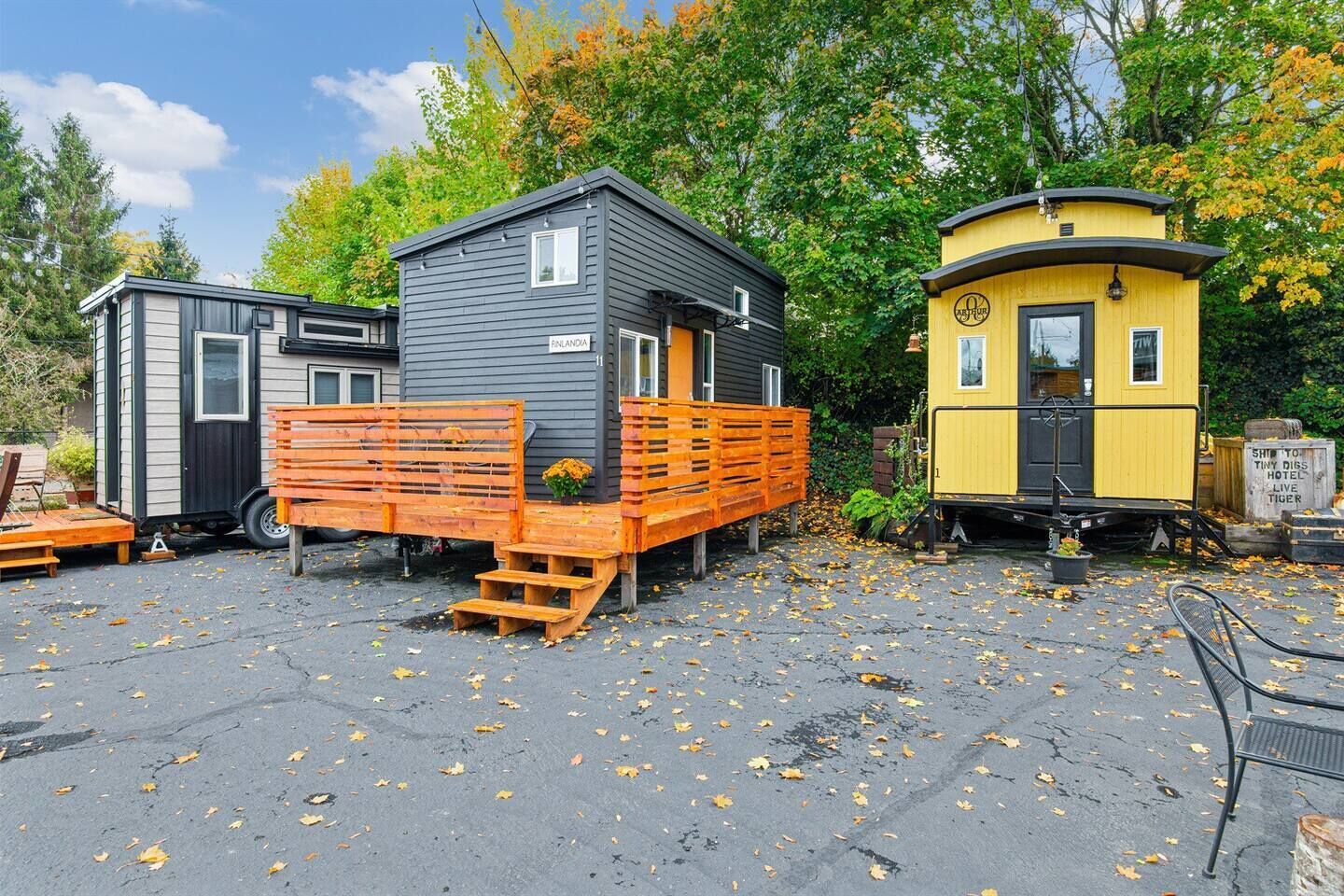 Kolme pientä mökkiä, joissa on puinen terassi ja portaat. Mökkien kylteissä lukee ”FINLANDIA” ja ”TINY DIGG HOTEL”.