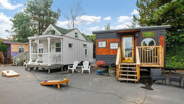 Two wooden houses with a porch and a deck, surrounded by outdoor seating and a small table. - The Modern - Custom Tiny Home w/ Modern Vibe (Portland)