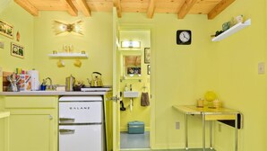 Une cuisine compacte avec un réfrigérateur Galanz d’époque, une petite table avec des tasses jaunes et une horloge au mur.