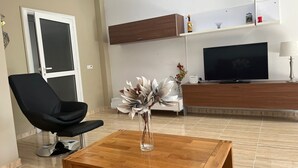 Ett vardagsrum med en svart fåtölj, ett soffbord i trä, en tv och en prydnadsväxt.