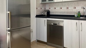 Ett modernt kök med vitvaror i rostfritt stål, ljusa träskåp och en kakelbeklädd vägg bakom arbetsbänken.