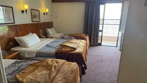 A hotel room with three beds, a wooden headboard, wall-mounted lights, and a balcony with a view. - St.Joseph Hotel (Luxor)