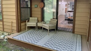 Ein überdachter Patio-Bereich mit zwei Korbstühlen und einer gemusterten Matte.