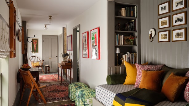 Een gezellige woonkamer met een bank, poefs, een boekenkast en een eethoek met een tafel en stoelen.