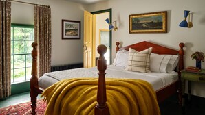 Een slaapkamer met een houten bed, een gele deken, een schilderij, een lamp en een raam met gordijnen.