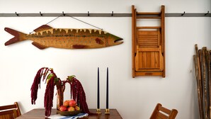 Een eethoek met een houten tafel, stoelen, een visdecoratie, een ladder en een plant met rode bloemen.