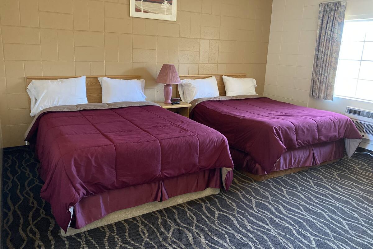 A hotel room with two beds, a nightstand, a lamp, and a framed picture on the wall.
