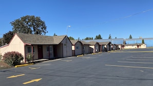 A row of single-story motel buildings with individual parking spaces. - Budget Inn Motel (Woodburn)