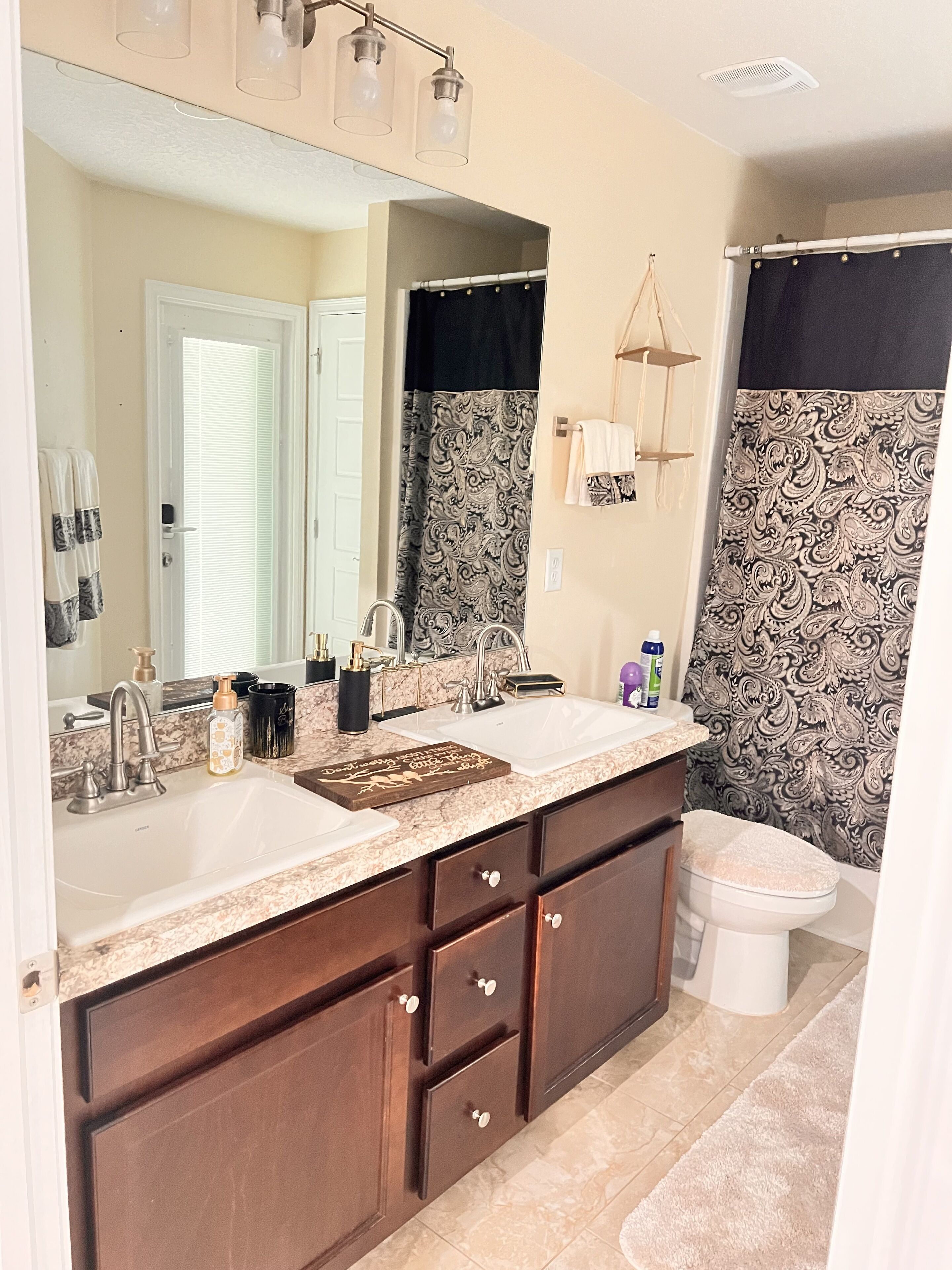 A bathroom with a double sink vanity, a toilet, and a shower curtain with a paisley pattern.