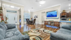 Amplia sala de estar con un televisor de pantalla plana grande, comedor con sillas y zona de cocina con armarios de madera y encimera.