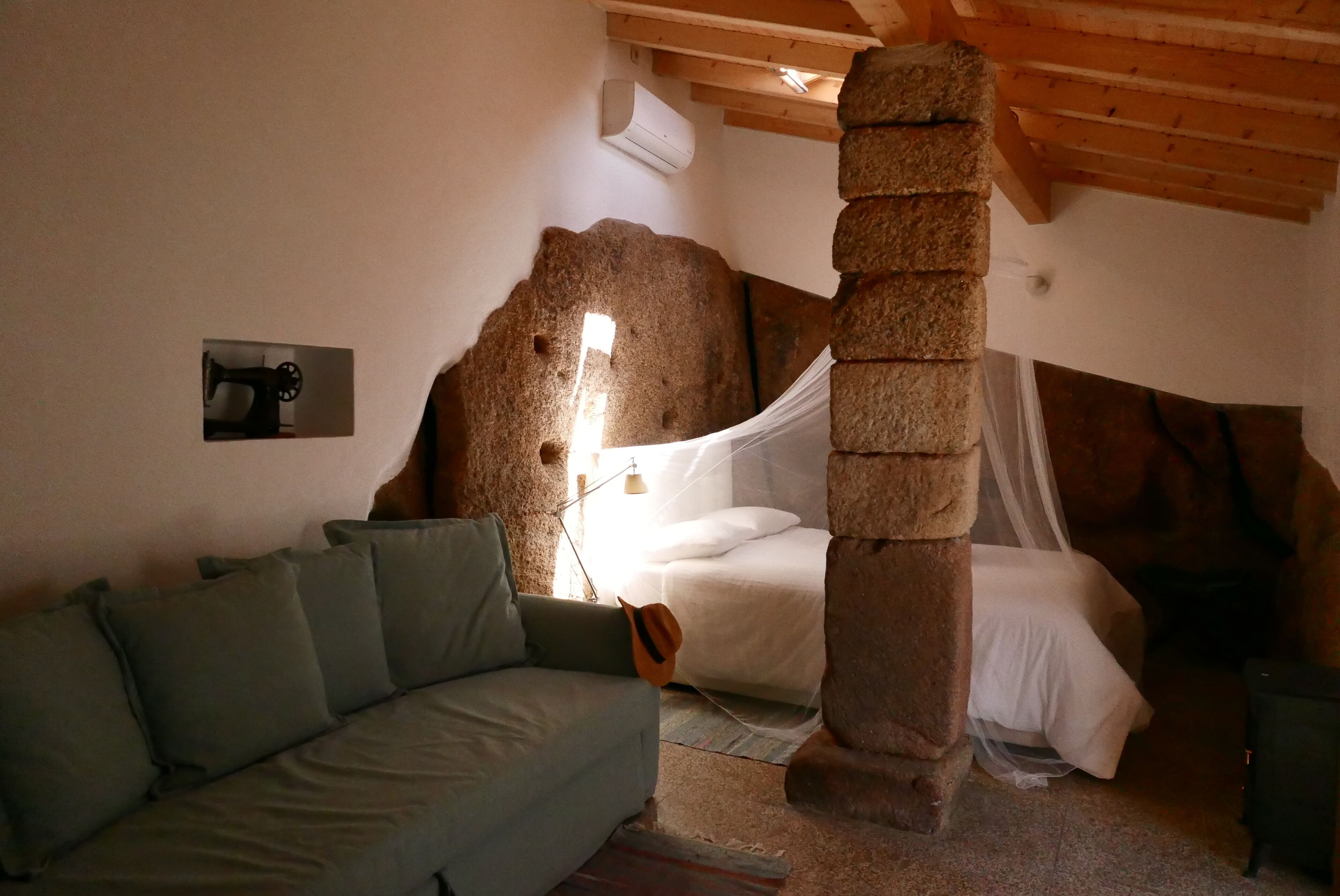 Une pièce rustique avec un mur en pierre, un lit recouvert de draps blancs, un canapé vert et un plafond en bois.
