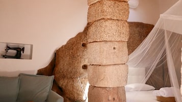 Quarto rústico com um pilar de pedra, uma cama com dossel, um sofá e uma máquina de costura na parede.
