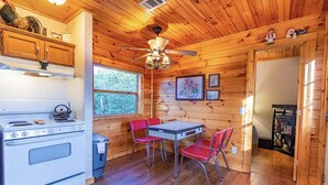 A cabin interior with a wooden interior, a dining table with red chairs, a stove, and a ceiling fan. -  Quiet hideout w/ Hot Tub & fire pit! BrysonCity! Pet Friendly! GSMR NOC  (Bryson City)