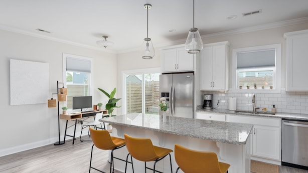 A modern kitchen with white cabinets, a stainless steel refrigerator, a granite countertop, and three yellow bar stools. - DT Oasis ~ Great Amenities, WFH Set-up, Outdoor Dining, Tennis & Pickleball (Wilmington)