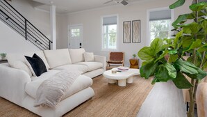 A modern living room with a white sofa, a coffee table, a ceiling fan, and a large plant. - DT Oasis ~ Great Amenities, WFH Set-up, Outdoor Dining, Tennis & Pickleball (Wilmington)