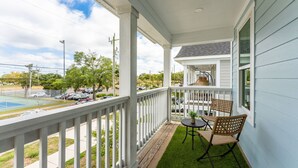 A covered porch with a view of a tennis court, a small table with chairs, and a potted plant. - DT Oasis ~ Great Amenities, WFH Set-up, Outdoor Dining, Tennis & Pickleball (Wilmington)