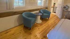 A cozy room with wooden floors, two blue armchairs, a small round table, and a bed with a white blanket.