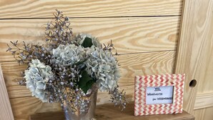 A wooden cabinet with a metal vase containing flowers and a sign with contact information.