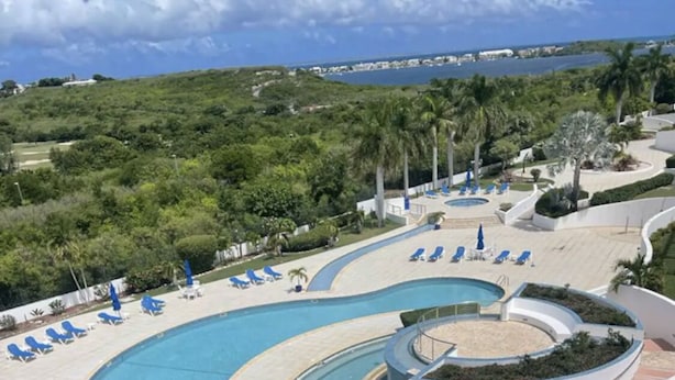 A resort with a large swimming pool, sun loungers, and a view of the ocean. - CONDO CORA. BLUE MARINE. SINT MAARTEN  (Sint Maarten)