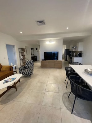 A modern living room with a sofa, a coffee table, a TV, and a dining area with chairs and a table.