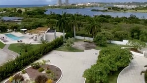 A resort with a pool, palm trees, and a view of a lake and city skyline. - CONDO CORA. BLUE MARINE. SINT MAARTEN  (Sint Maarten)