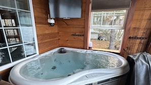 A wooden cabin with a hot tub, a TV mounted on the wall, and a view of the outdoors.