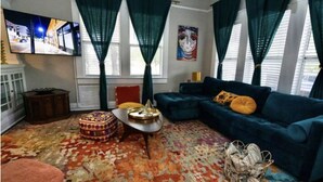 Un salón con un sofá azul, una alfombra estampada y un televisor en la pared.