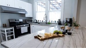 Una cocina moderna con armarios blancos, una isla central con encimera de mármol y un amplio ventanal que aporta luz natural.