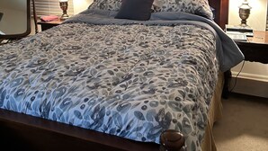 A bedroom with a bed, two bedside lamps, a nightstand, a mirror, and a window with blinds. - The Villages
Lake Sumpter
Most desirable area 
Golf, pools and music every night (The Villages)