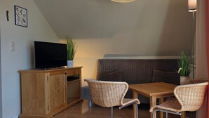 A cozy room with a wooden TV stand, wicker chairs, a small table, and a cushioned bench.