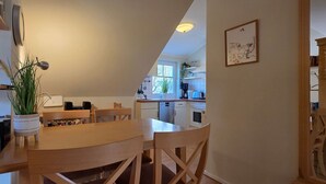 A cozy kitchen with a wooden dining table and chairs, a potted plant, and a view of the adjacent dining area.