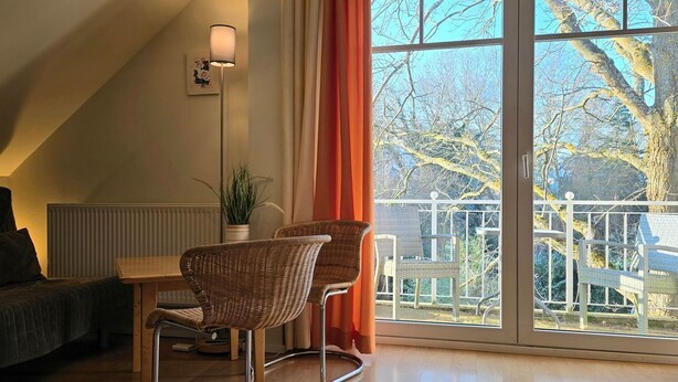 A cozy living area with a sofa, a dining table, and two chairs. A large window offers a view of the outdoors, including a tree and a fence.