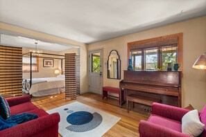 A spacious room with a wooden floor, a red sofa, a blue sofa, a wooden piano, and a bed with a striped headboard. - Adorable Santa Fe 3 Bedroom Home! (Santa Fe)