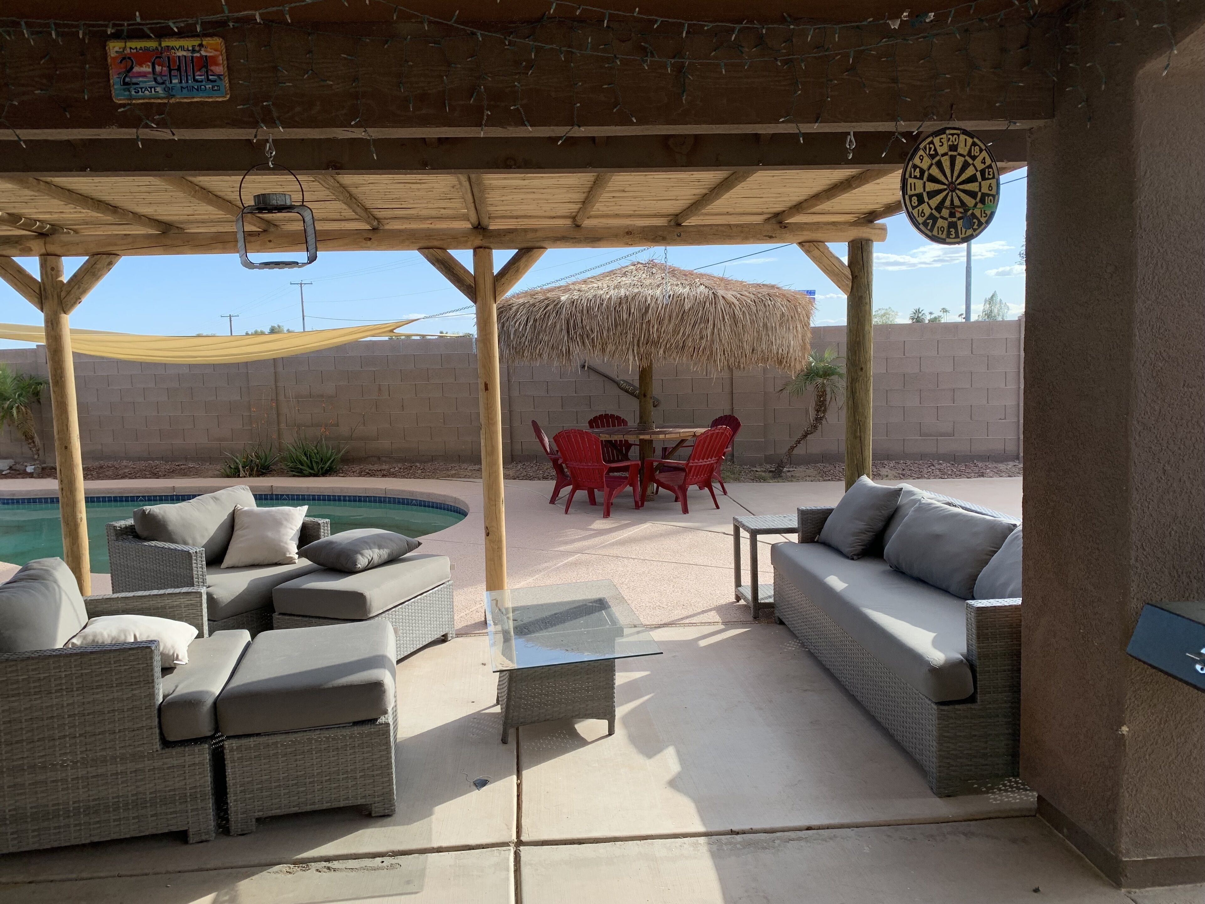 Une terrasse extérieure couverte, aménagée avec des meubles en osier, une piscine et un parasol en chaume.