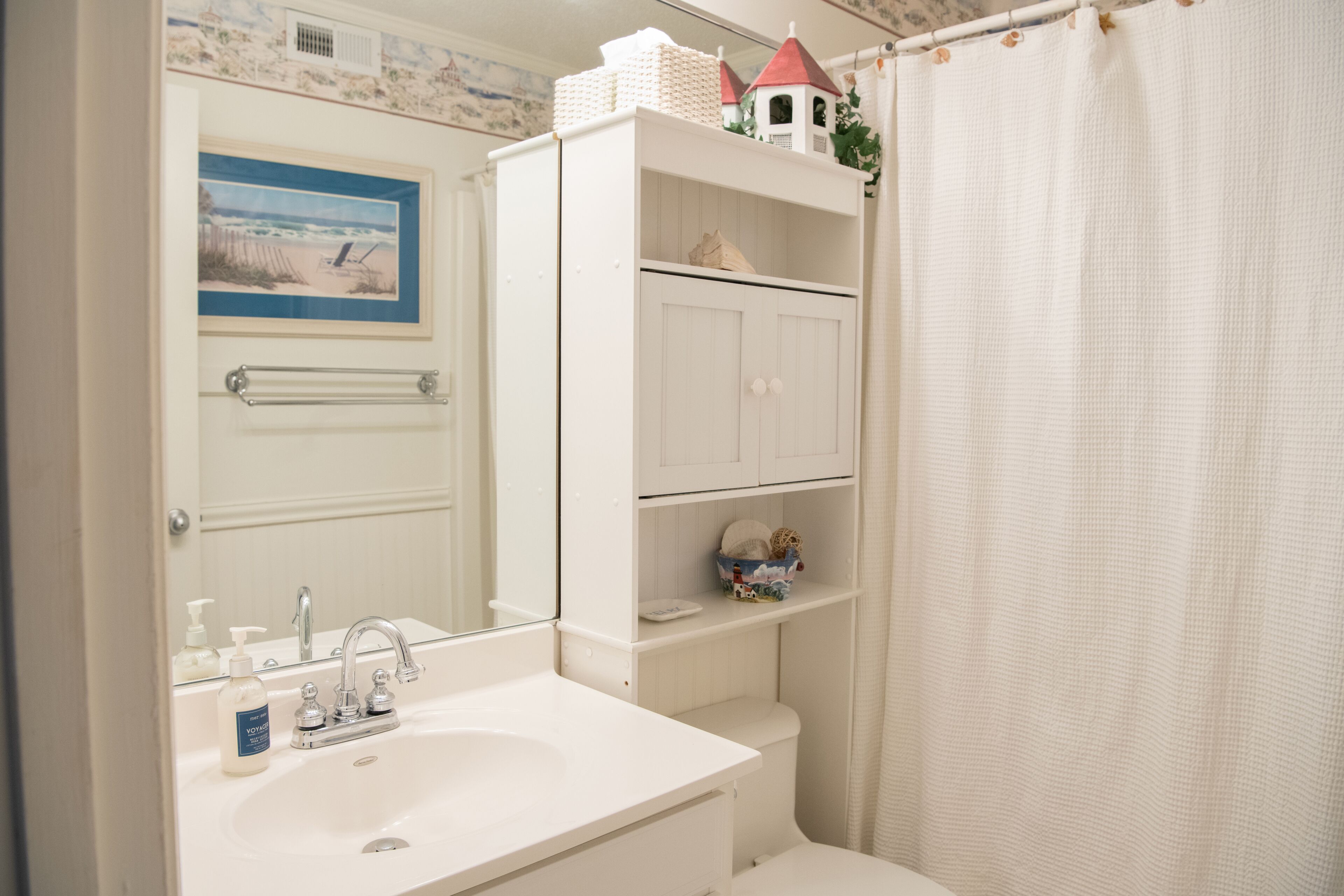 A bathroom with a white sink, a mirror, a toilet, and a shower curtain.