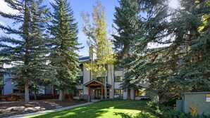 A building with a modern architectural style, surrounded by tall evergreen trees and a well-maintained lawn. - TRUE SKI IN / SKI OUT, POOL, HOT TUB, GYM, TENNIS COURTS, CLOSE TO DOWNTOWN (Park City)