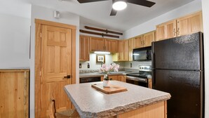 A kitchen with wooden cabinets, a black refrigerator, a granite countertop, and a ceiling fan. - TRUE SKI IN / SKI OUT, POOL, HOT TUB, GYM, TENNIS COURTS, CLOSE TO DOWNTOWN (Park City)