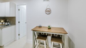 A kitchen with white cabinets, a granite countertop, and a wooden dining table with two stools. - Adorable Studio (Miami)