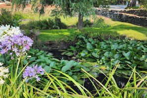 A garden with a pond, surrounded by greenery and a stone wall. - The Lily Pond House-Walk to Beach, SPA, Sleeps 6 (Gold Beach)