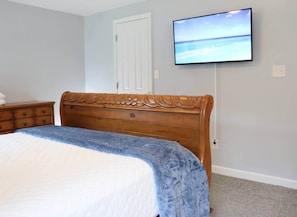 A bedroom with a wooden bed, a nightstand, a TV on the wall, and a door. - 3BR Pet-Friendly Retreat near Camp Lejeune (Jacksonville)